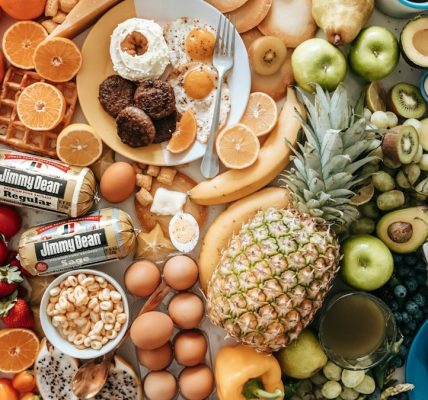A large assortment of fresh fruit, eggs, breakfast meats, and donuts on a table