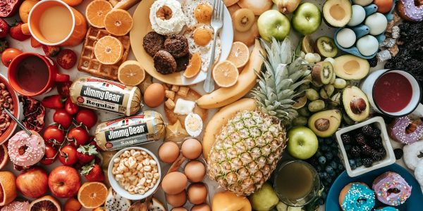 A large assortment of fresh fruit, eggs, breakfast meats, and donuts on a table